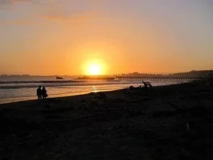 A sunset over the ocean with people on the beach.